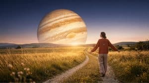 Golden banded planet Jupiter glowing above an open landscape at dawn with a woman walking toward it